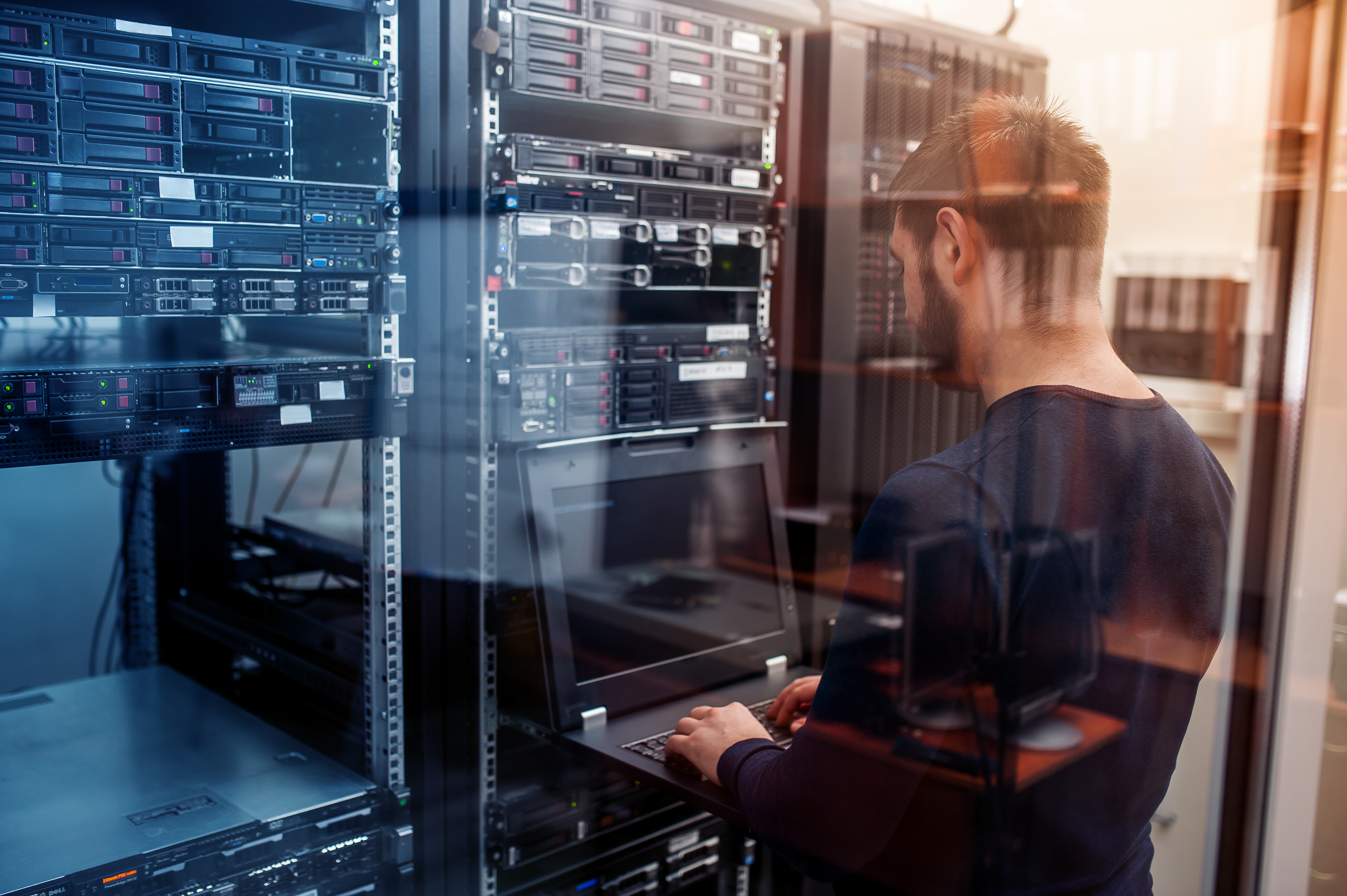 Mann, der in einem Server-Raum am Computer arbeitet